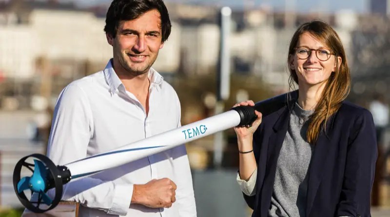 A man and woman hold a TEMO electric boat motor on a stick. It is about 5 feet / 1.5 metres long and 4 inches / 10 cm in diameter